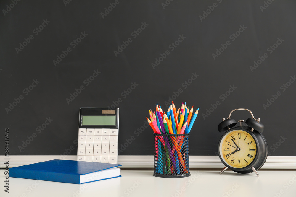 Set of school stationery with alarm clock on table in classroom