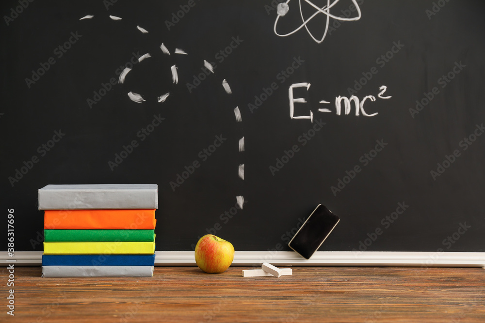 Books with chalk and apple on table near chalkboard in classroom