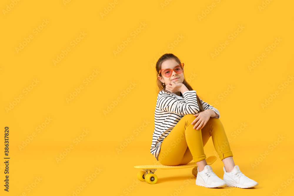 Cute little girl with skateboard on color background