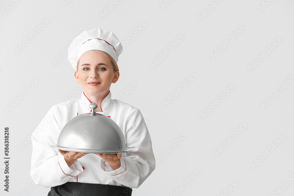 Mature female chef with tray and cloche on grey background