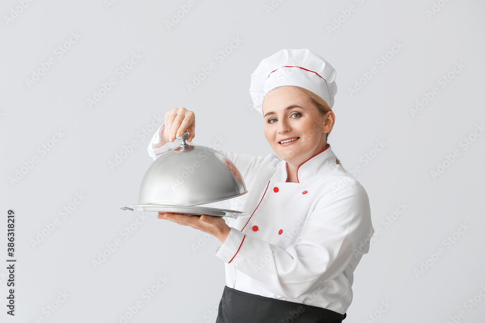 Mature female chef with tray and cloche on grey background