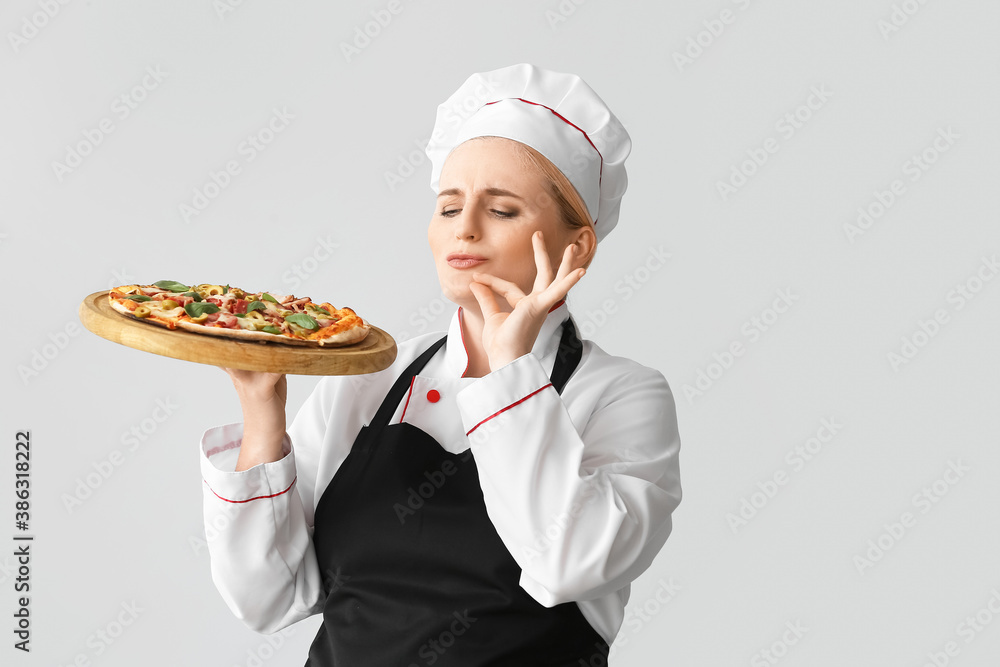 Mature female chef with tasty pizza on grey background