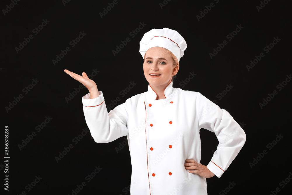 Mature female chef showing something on dark background