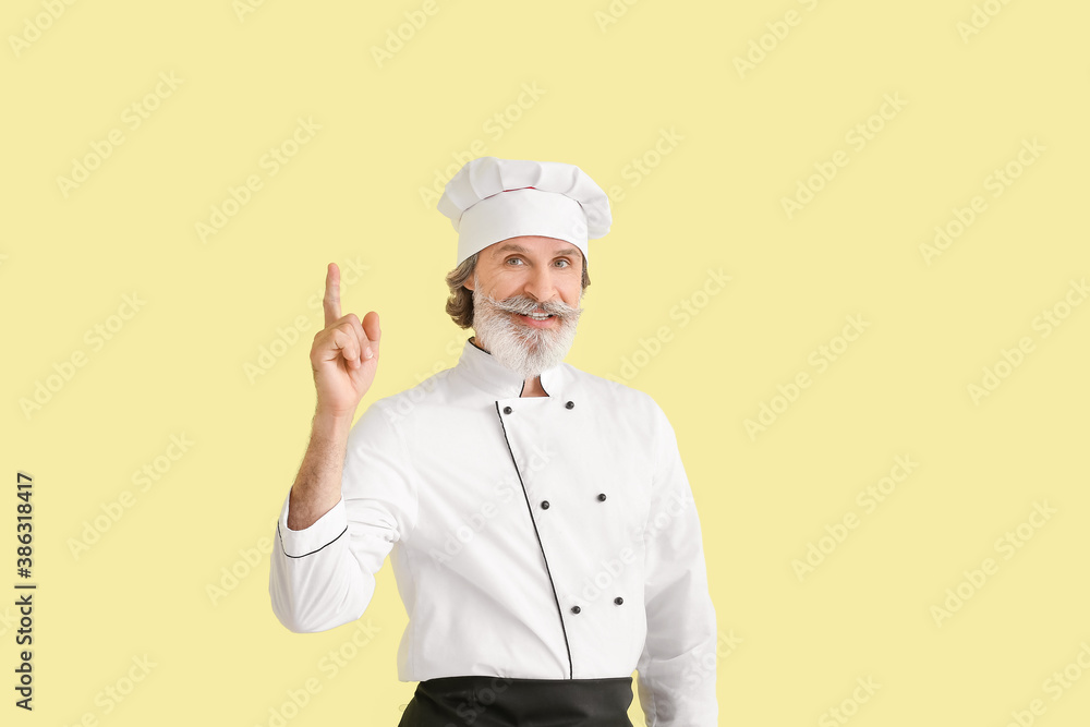 Mature male chef with raised index finger on color background