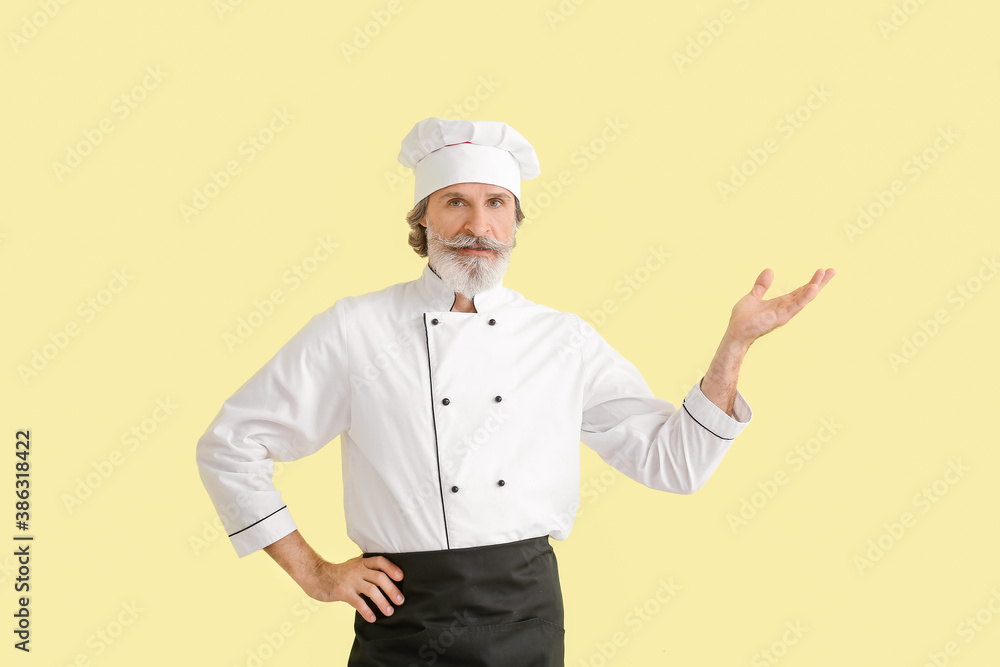 Mature male chef showing something on color background