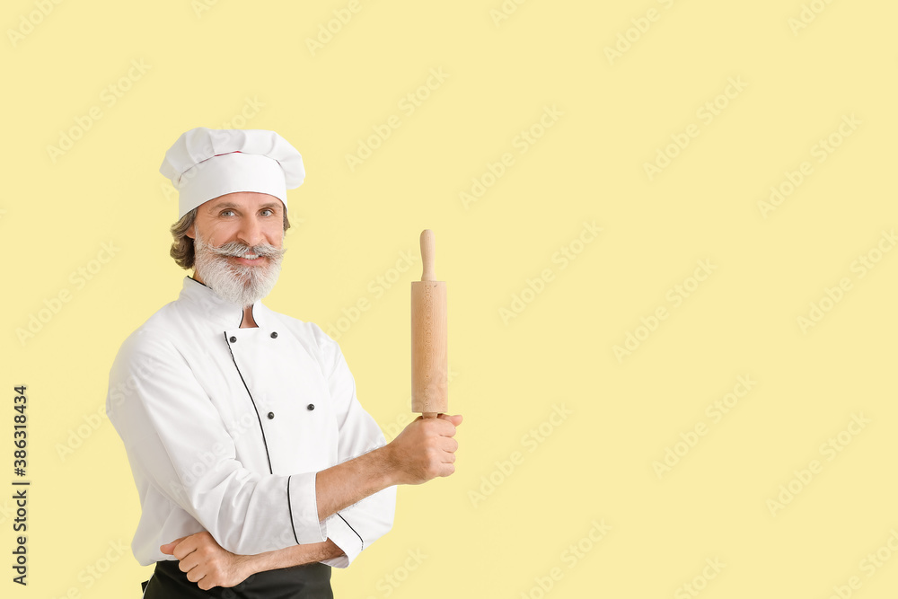 Mature male chef with rolling pin on color background