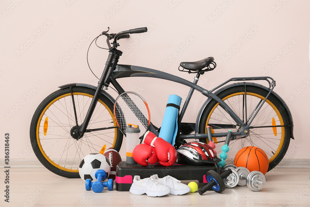 Set of sport equipment with bicycle near light wall