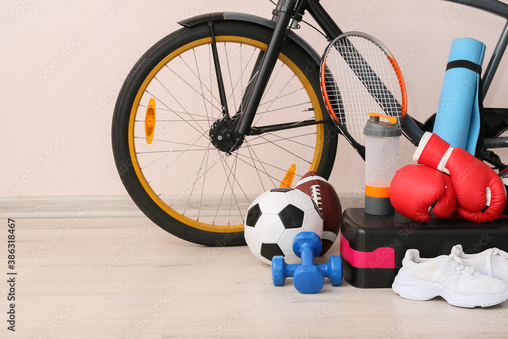 Set of sport equipment with bicycle near light wall