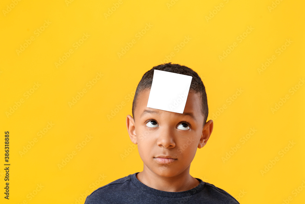 Little African-American boy with blank note paper on his forehead against color background