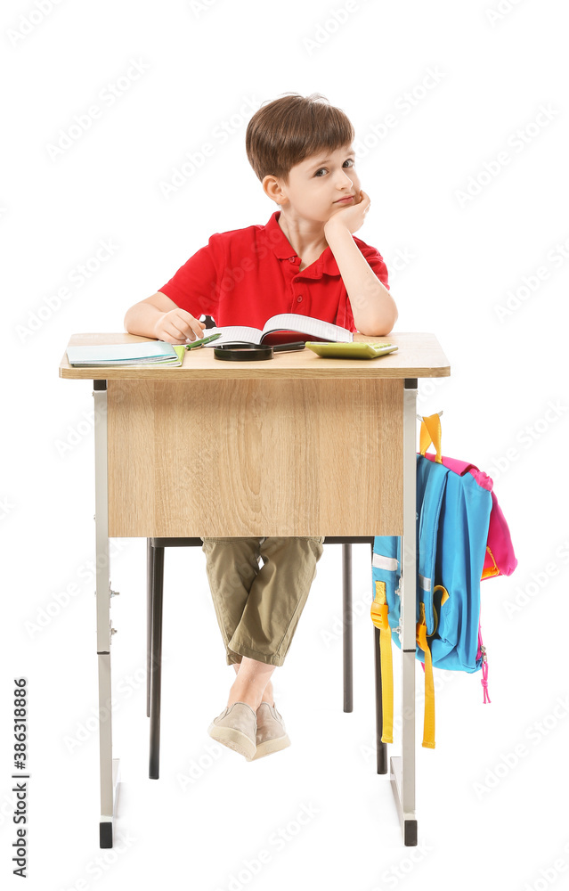 Little pupil sitting at school desk against white background