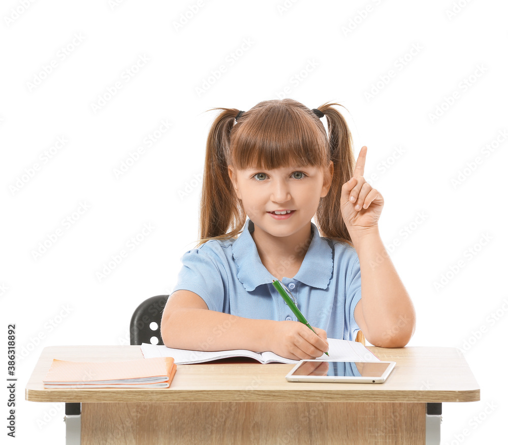 Little pupil with raised index finger sitting at school desk against white background