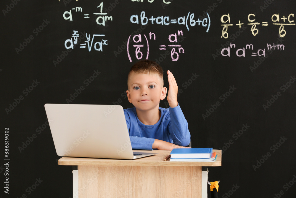 Cute pupil with raised hand sitting at desk during lesson in classroom