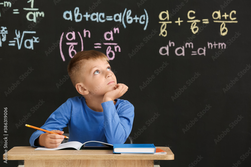 Cute pupil sitting at desk during lesson in classroom