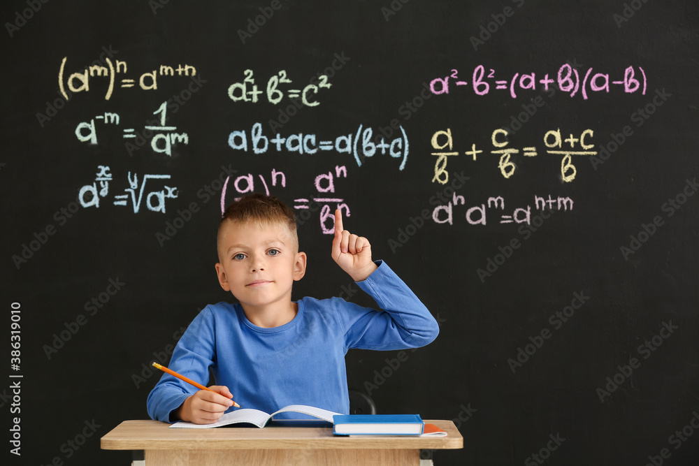 Cute pupil with raised index finger sitting at desk during lesson in classroom