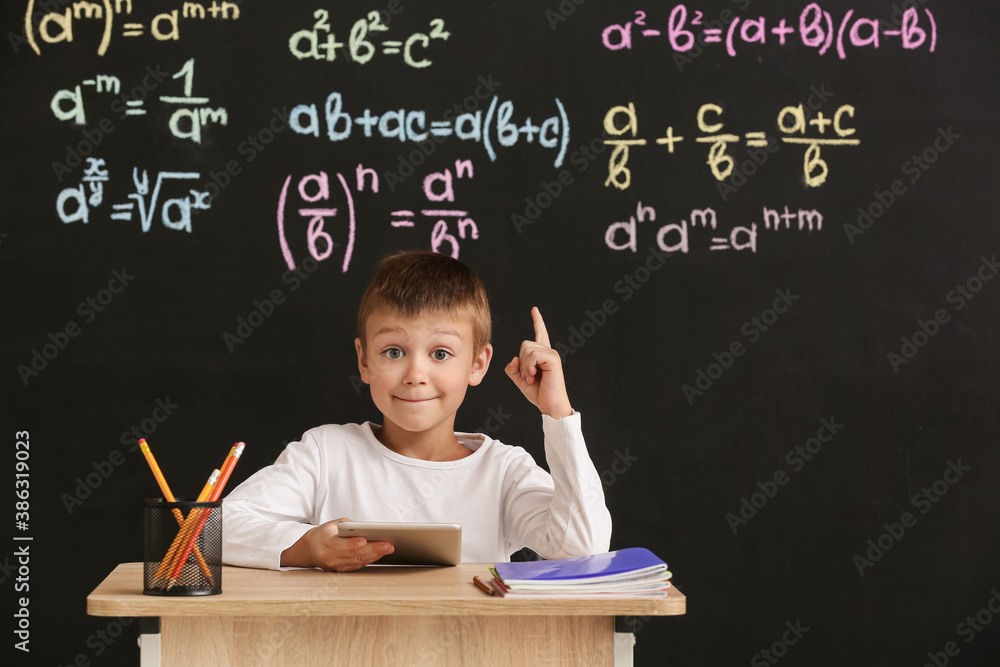 Cute pupil with raised index finger sitting at desk during lesson in classroom