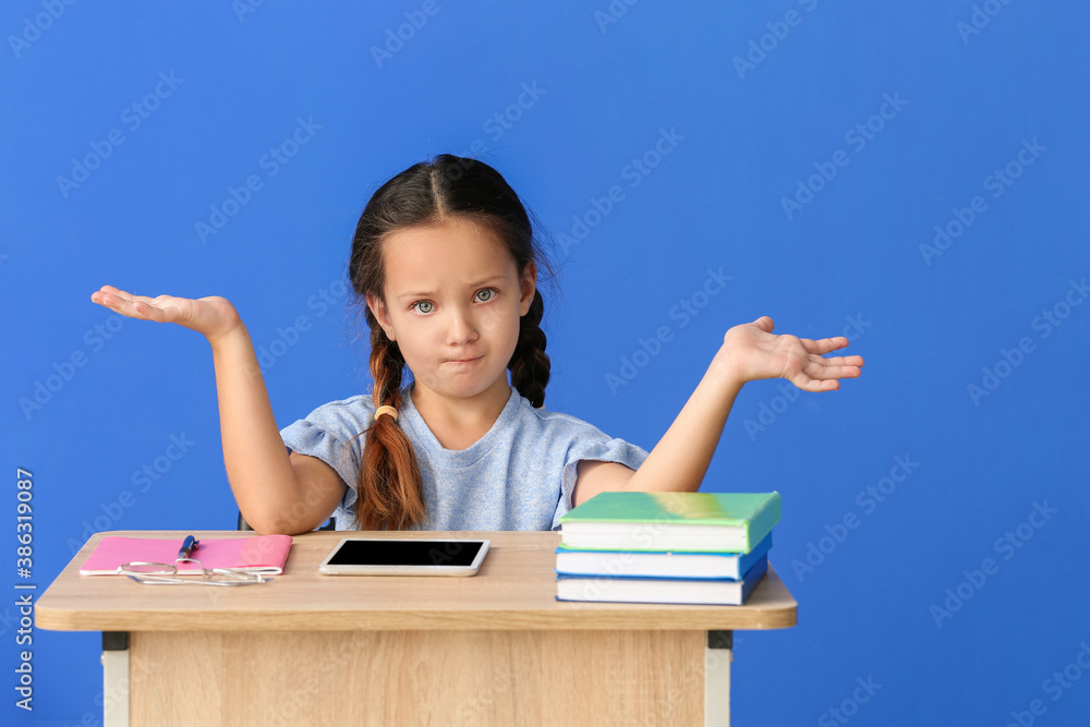 Confused pupil sitting at desk against color background