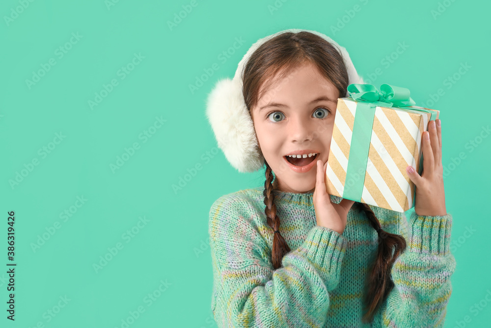 Surprised little girl with Christmas gift on color background