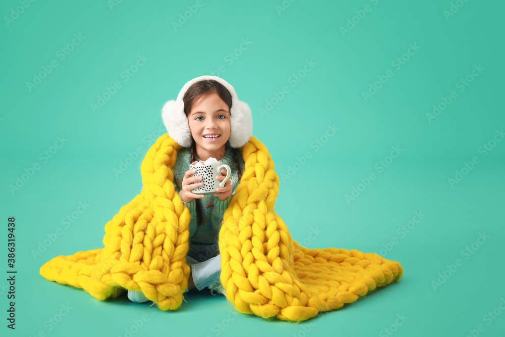 Cute little girl with warm plaid and cup of hot chocolate on color background