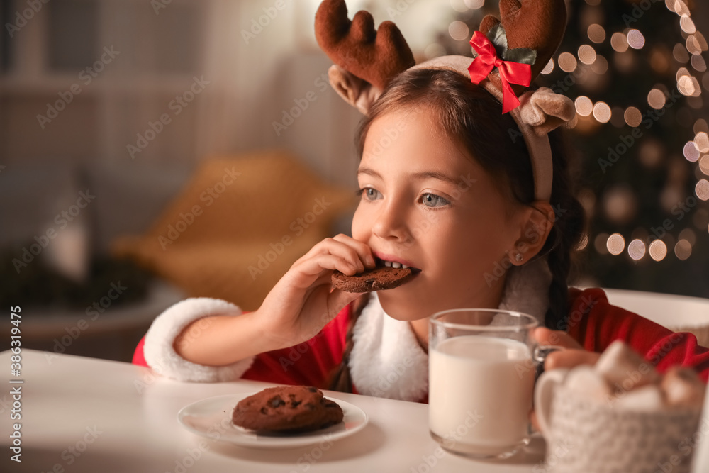 Cute little girl drinking milk with cookies at home on Christmas eve