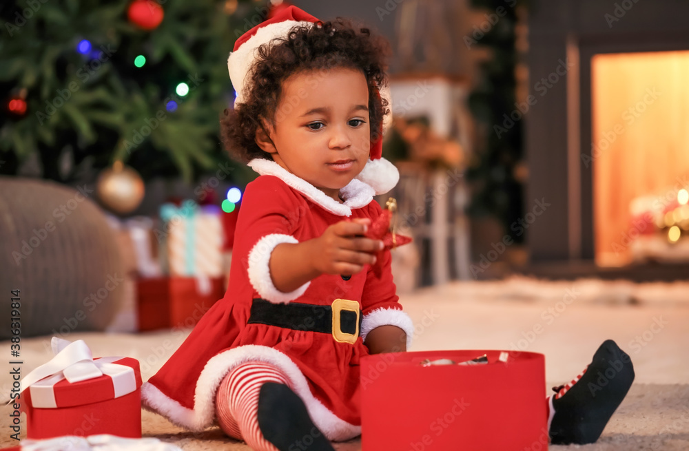 Cute African-American baby girl with gift at home on Christmas eve