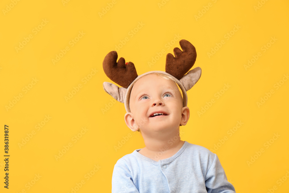 Cute little baby with deer horns on color background