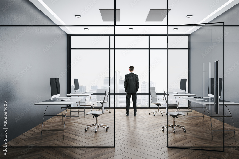 Businessman in suit standing in office with computers on table