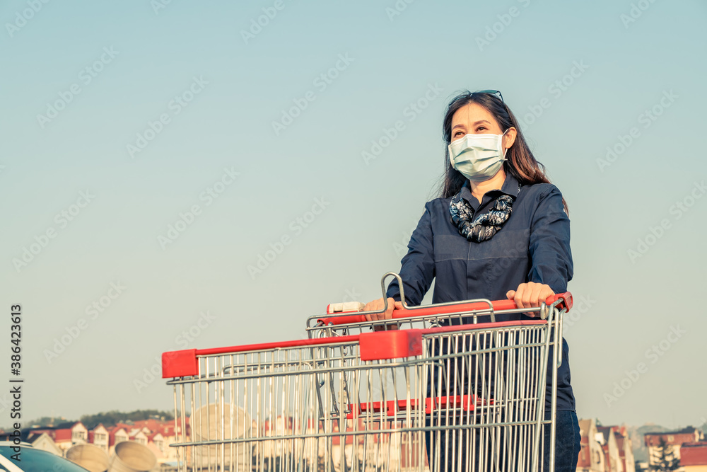 Woman shopping with hand pushing cart in supermarket parking lot