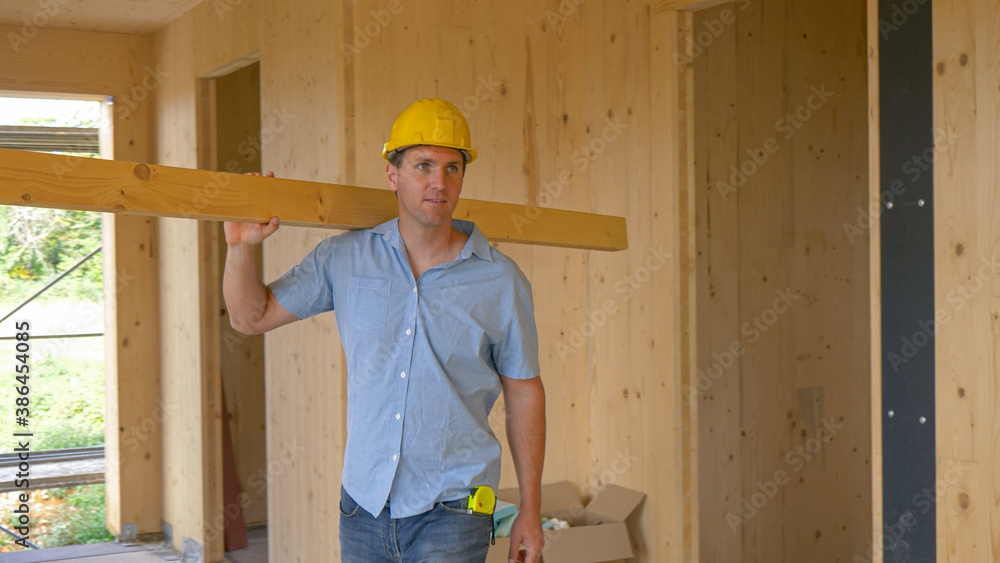 CLOSE UP: Happy carpenter carrying a long plank looks around the CLT house.