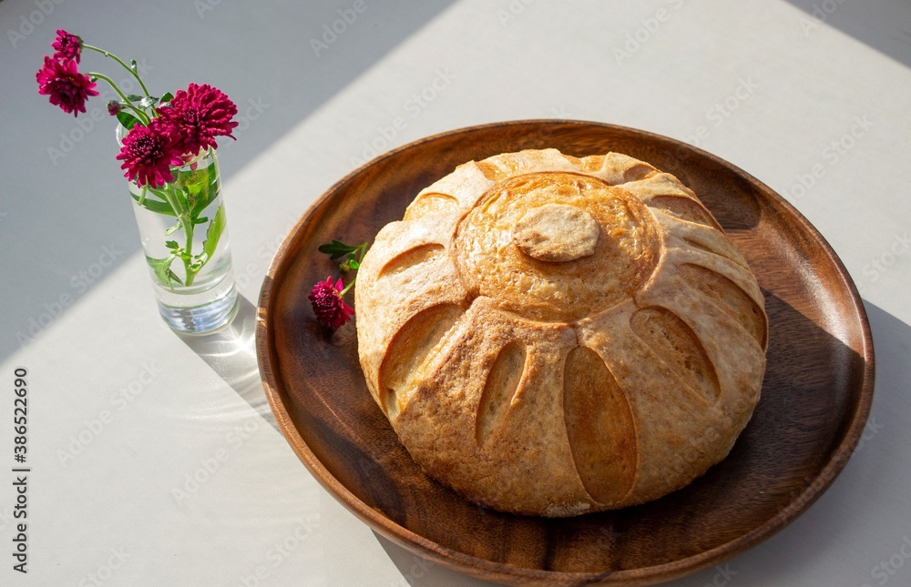 Composition in natural light. Homemade bread (French bun) on a dark wood plate, in the sun. And a re