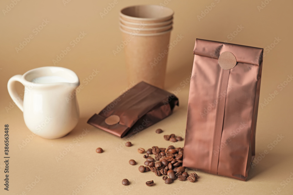 Coffee bags, cup and jug of milk on color background