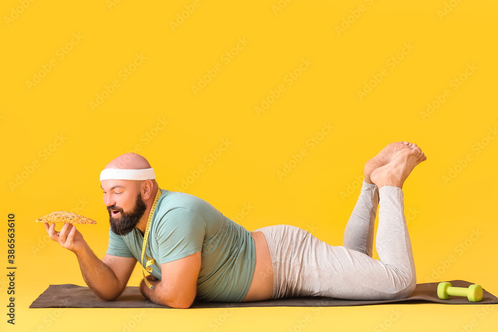 Overweight man in sportswear and with pizza on color background