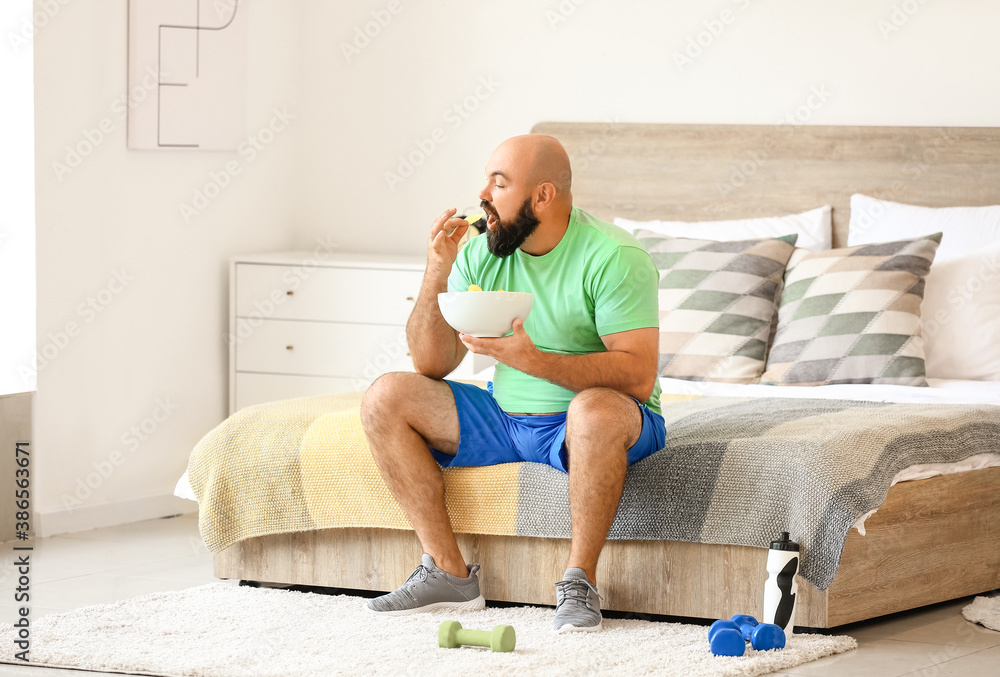 Overweight man eating chips at home. Weight loss concept