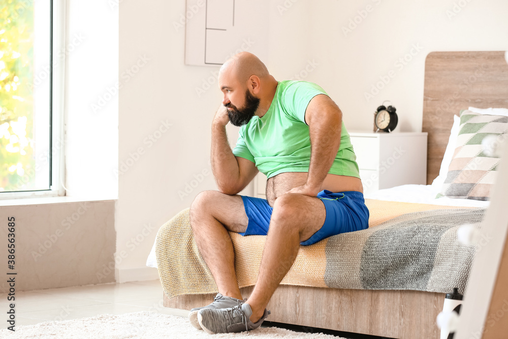 Sad overweight man sitting on bed at home. Weight loss concept