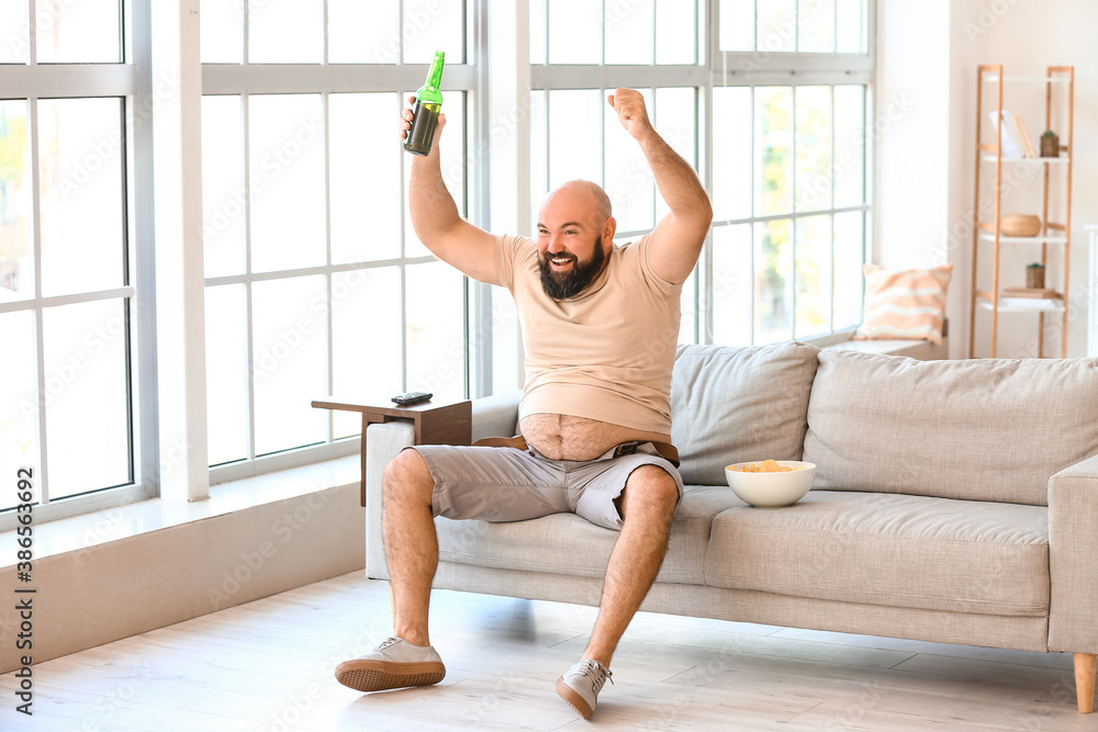 Lazy overweight man with beer and chips watching TV at home