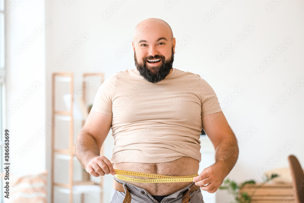 Happy overweight man measuring his waist at home. Weight loss concept