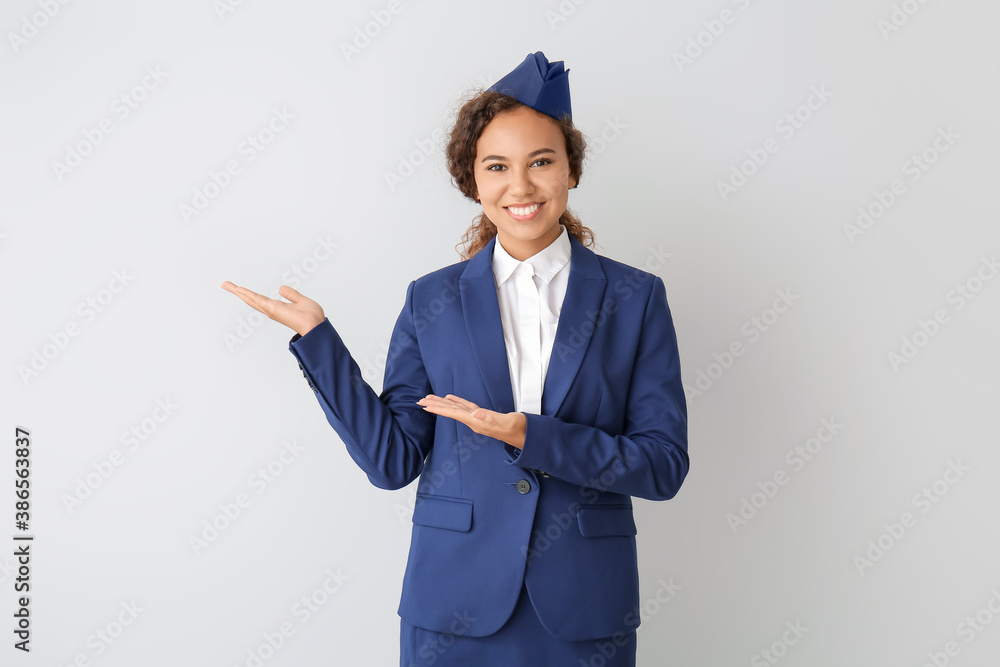 Beautiful African-American stewardess showing something on grey background