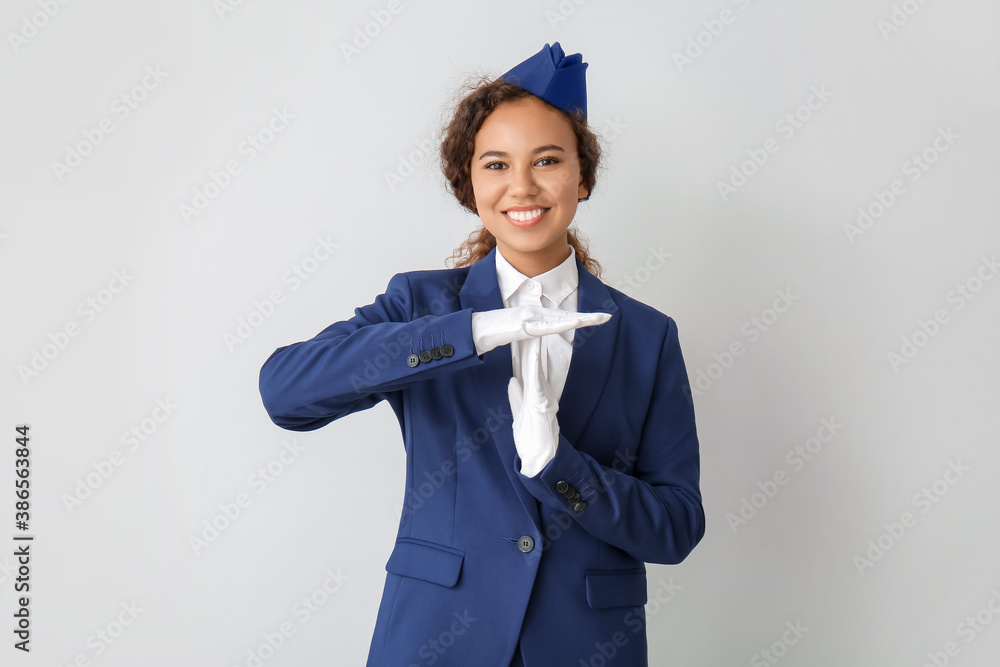 Beautiful gesturing African-American stewardess on grey background