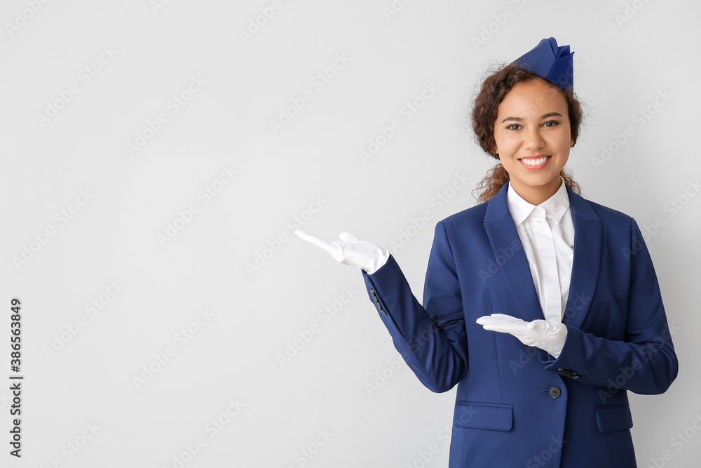 Beautiful African-American stewardess showing something on grey background