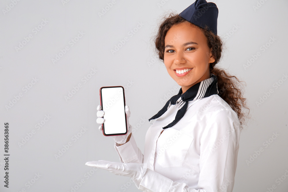 Beautiful African-American stewardess with mobile phone on grey background