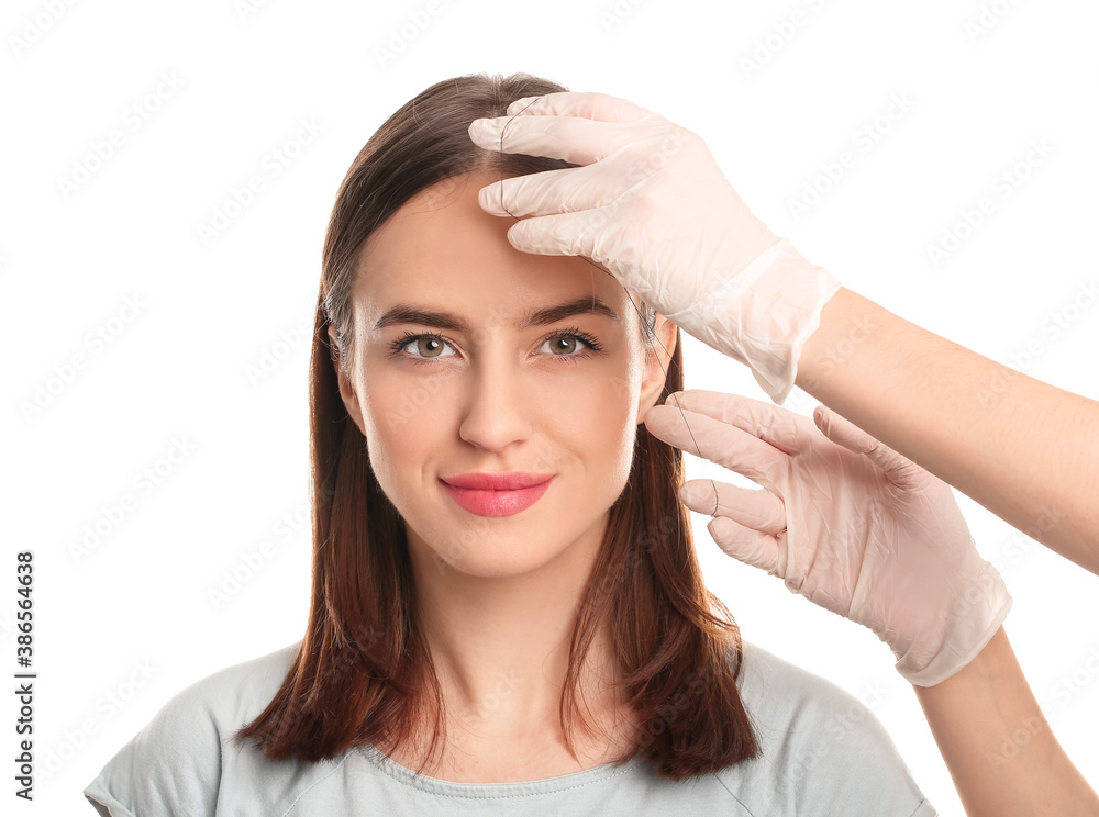 Young woman undergoing eyebrow correction procedure on white background