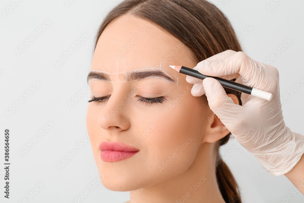 Young woman undergoing eyebrow correction procedure on light background