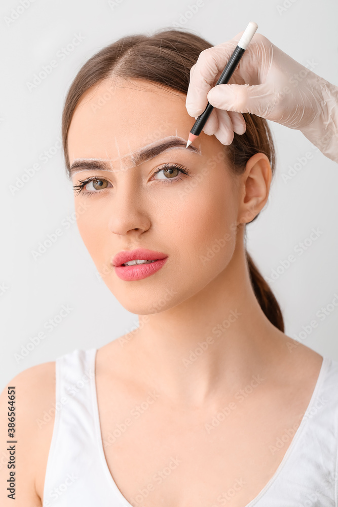 Young woman undergoing eyebrow correction procedure on light background