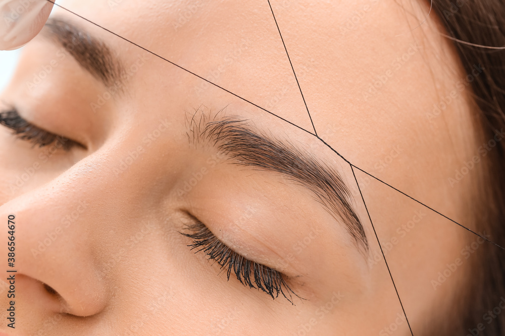 Young woman undergoing eyebrow correction procedure in beauty salon, closeup