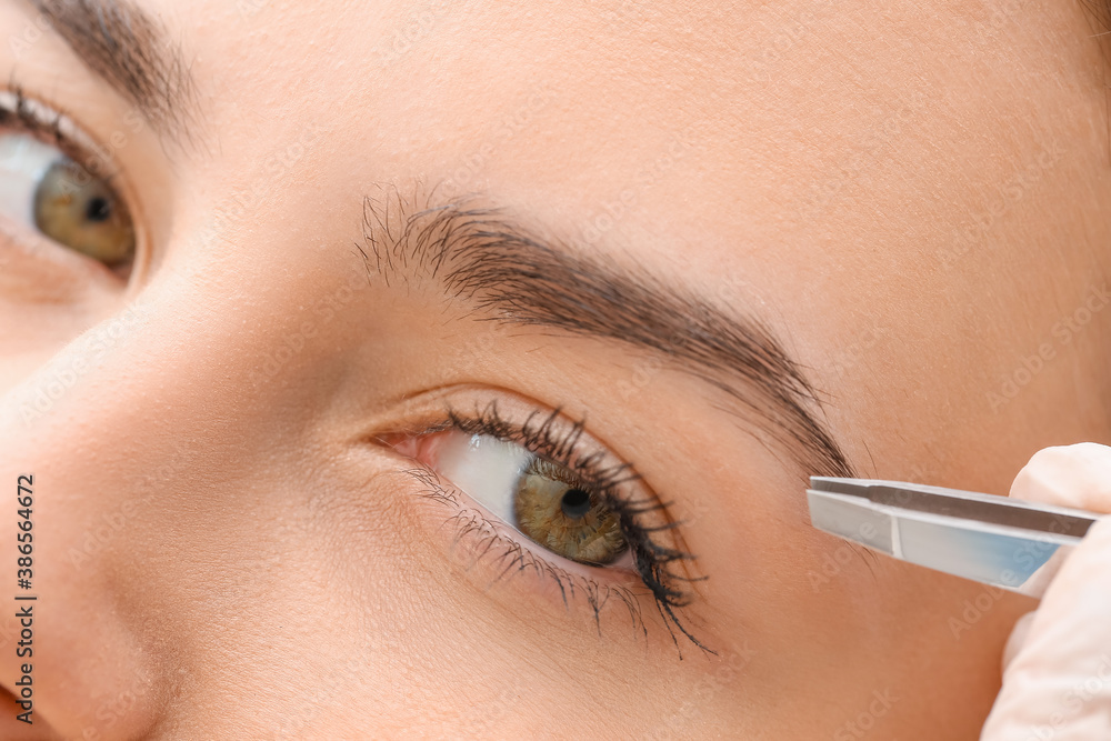 Young woman undergoing eyebrow correction procedure in beauty salon, closeup