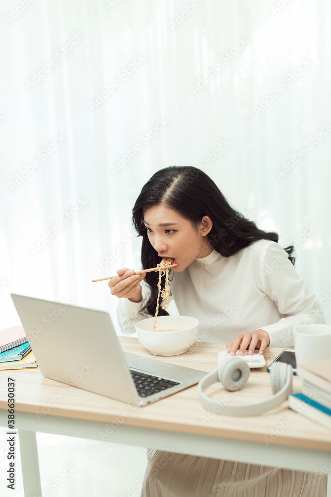 Asia freelance business woman eating instant noodles while working on laptop in living room at home 