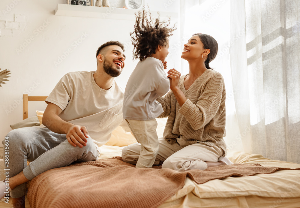 happy diverse family mom, dad and child  laughing, playing and jumping   in bed   at home.