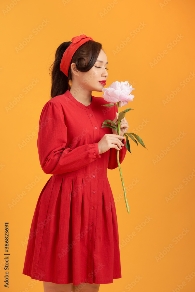 Close up young Asian woman holding peony flower over orange background.