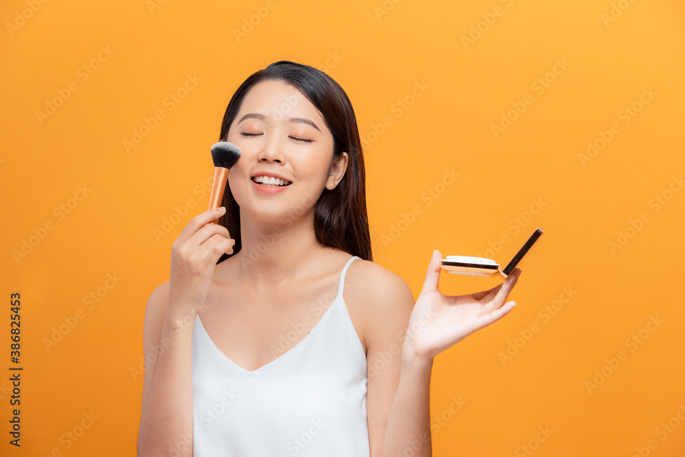 Close up asian woman apply cosmetic brush over yellow background .