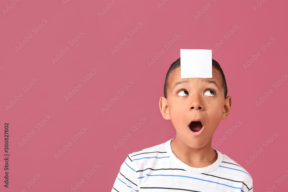 Little African-American boy with blank note paper on his forehead against color background