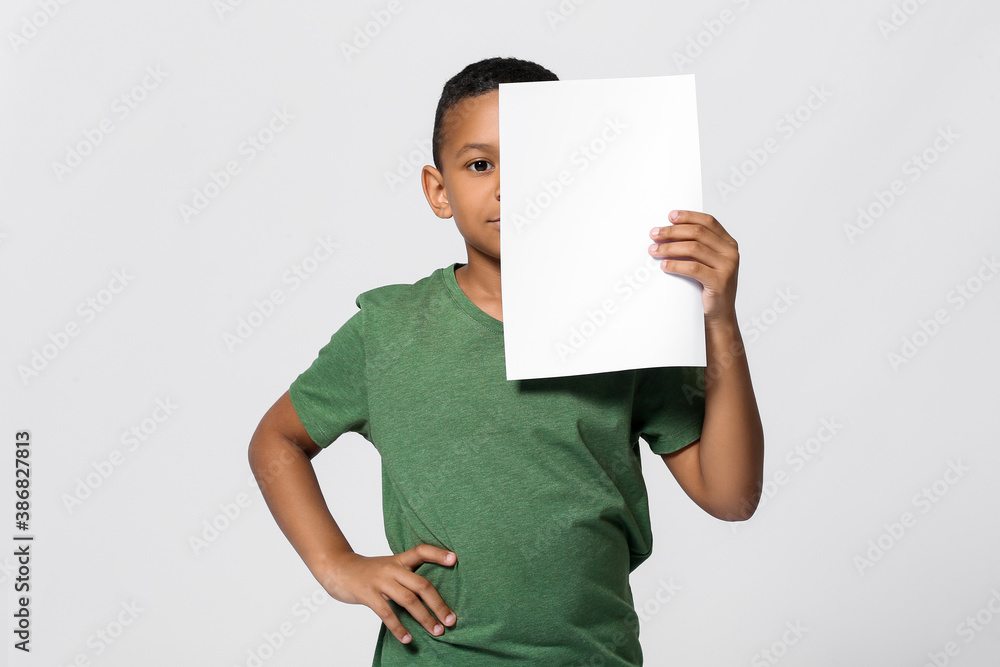 Little African-American boy with blank paper sheet on light background